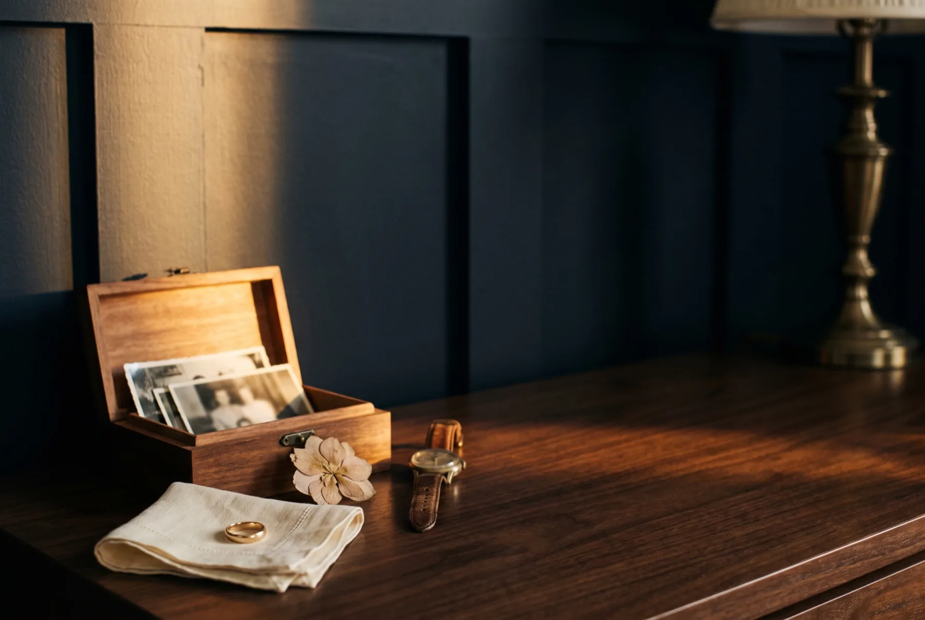 An open memory box of old family photographs, a wedding ring, a pressed flower and a wristwatch.