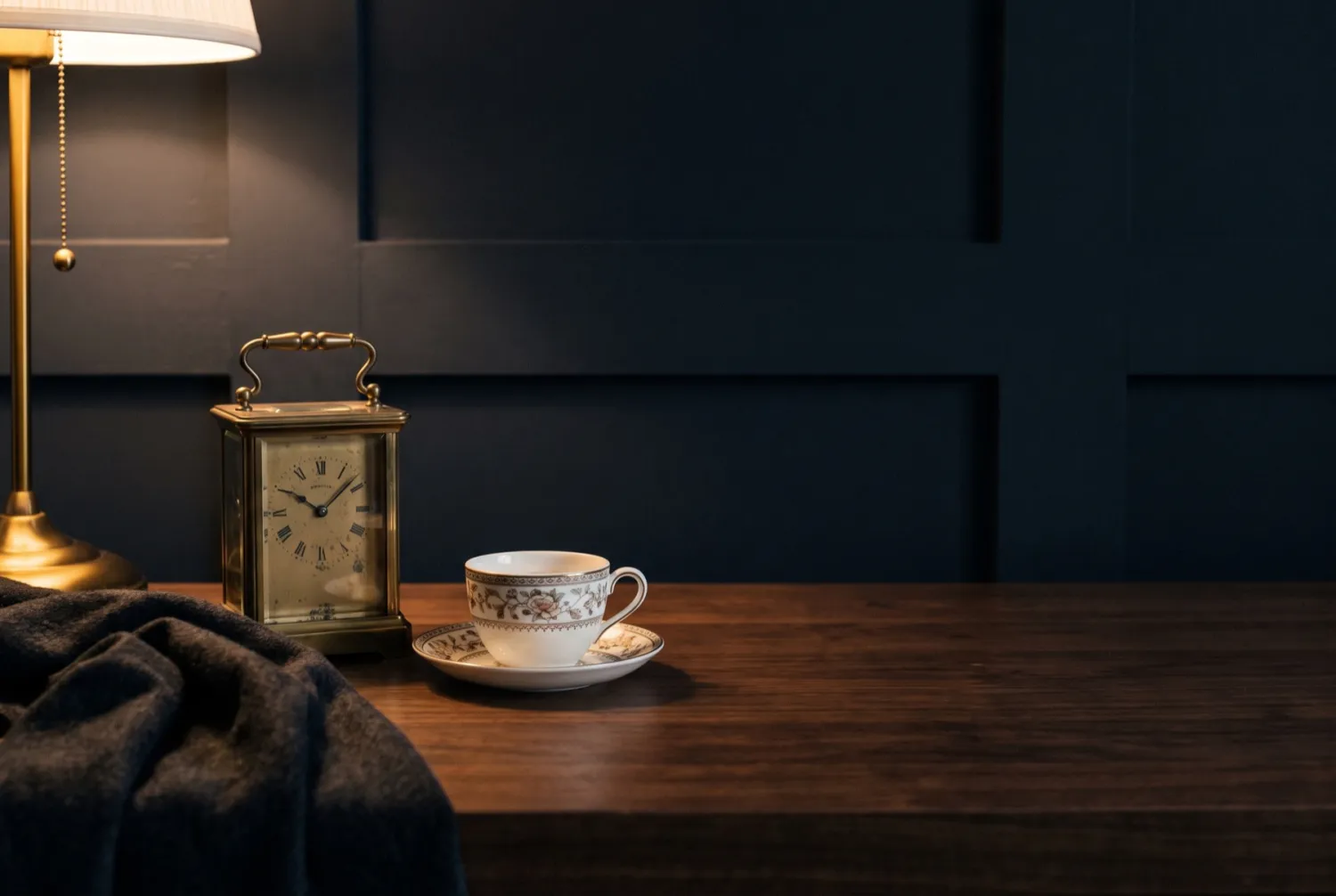 A small carriage clock, a folded shawl and a china teacup arranged in a new room.